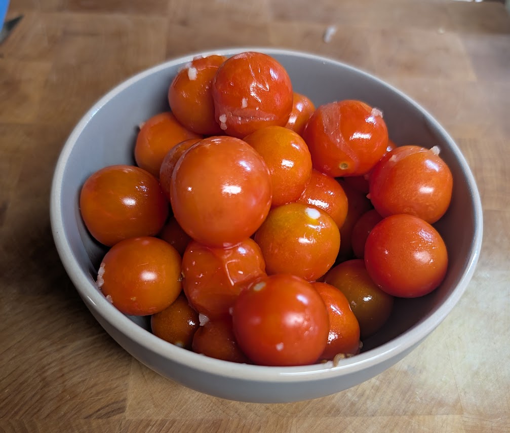 A stoneware bowl full of fermented cherry tomatoes on a wooden cutting board